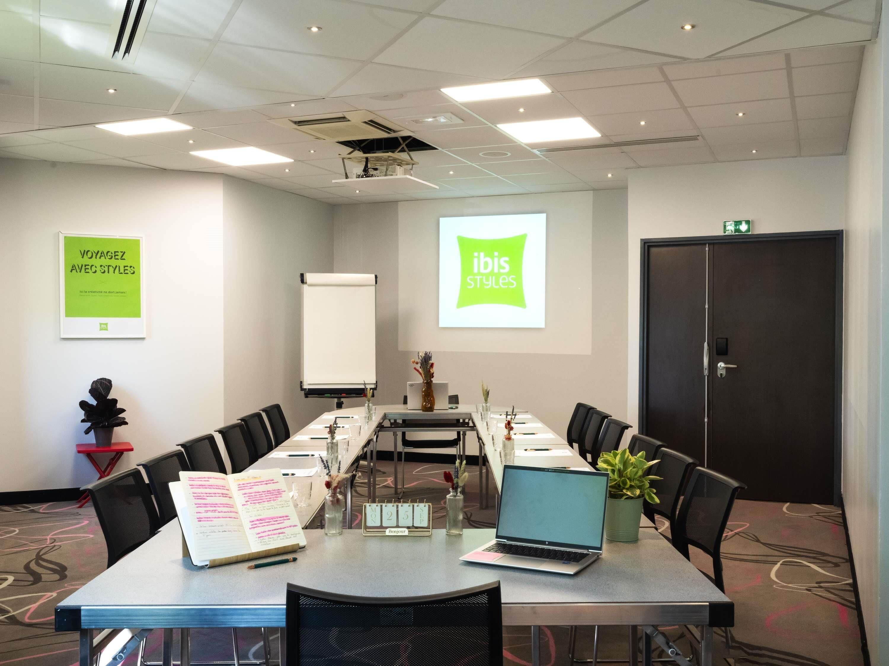 A conference room with a long table, chairs, a laptop, a projector screen, and a door.