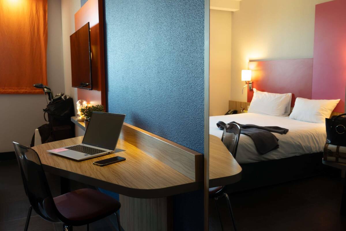 A hotel room with a desk, laptop, chair, bed, and bedside table.