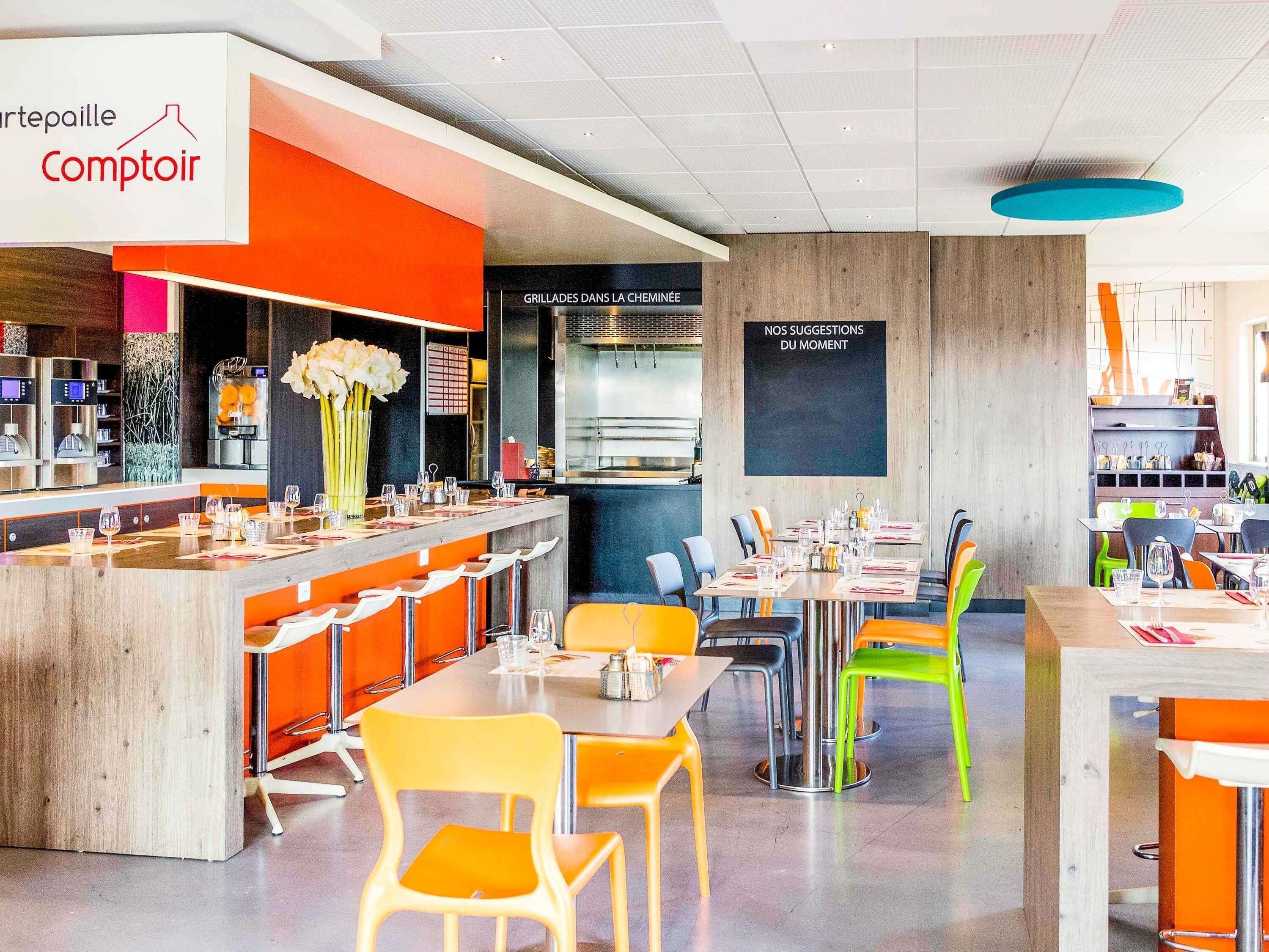 Een restaurant met een bar, meerdere eettafels en stoelen.