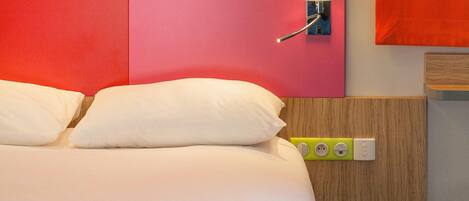 A hotel room with a bed, a bedside lamp, a green power strip, and a red chair.