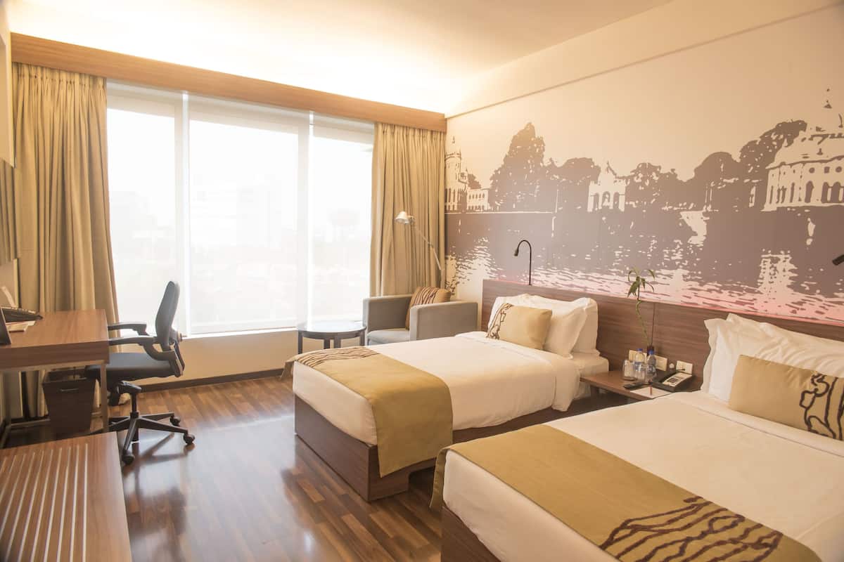 Une chambre d’hôtel avec deux lits, un bureau, une chaise, une petite table et une grande fenêtre avec des rideaux.