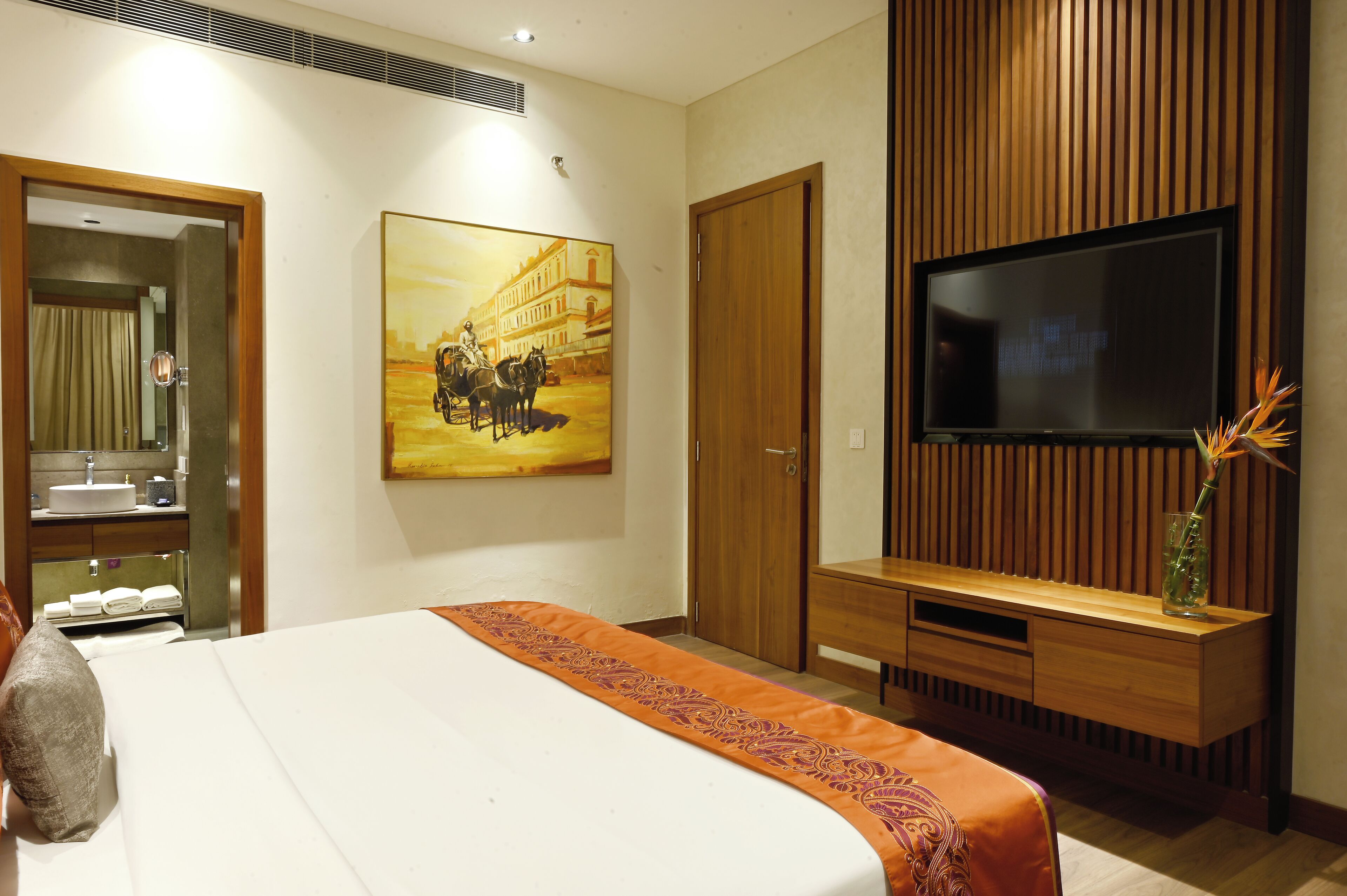 A hotel room with a large bed, a TV mounted on the wall, a wooden panel design, and a painting on the wall.