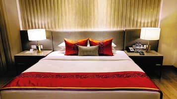 Quarto de hotel com uma cama grande, duas mesas de cabeceira com abajures e uma cabeceira com persianas verticais.