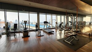 A gym with various exercise equipment, large windows, and a wooden floor.