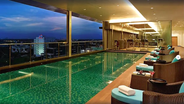 A rooftop infinity pool with a city view, sun loungers, and a bar area.