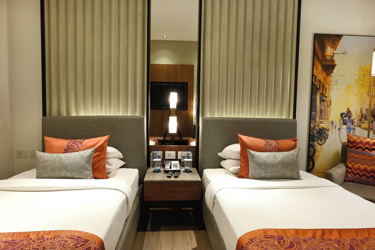 Une chambre d’hôtel avec deux lits, une table de chevet avec une lampe, un miroir et un tableau au mur.