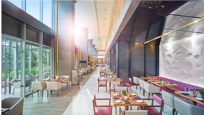 A modern restaurant with high ceilings, large windows, and a mix of seating arrangements including tables and booths.