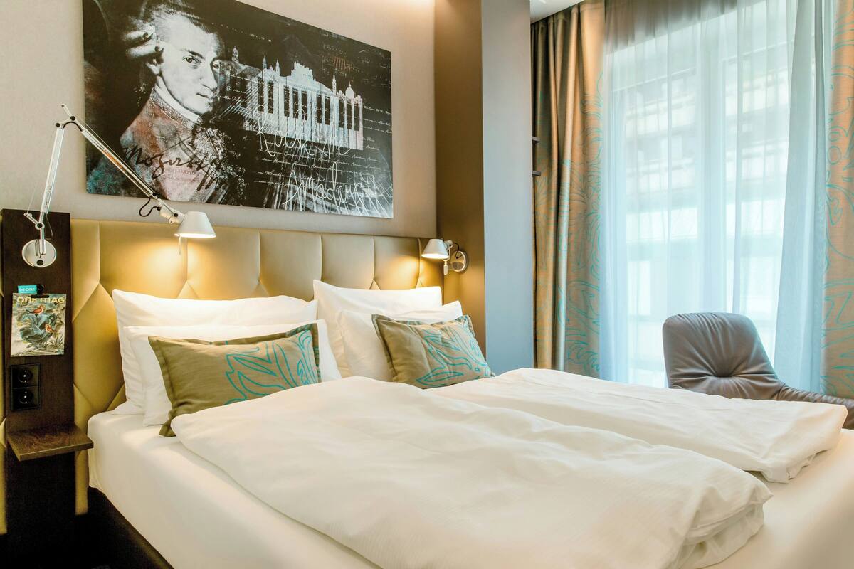 Una habitación de hotel con una cama grande, dos lámparas de noche, una mesita de noche y una obra de arte colgada en la pared.