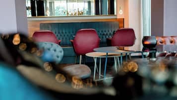 Un interior moderno con una zona de estar que incluye un banco acolchado azul y sillas rojas, una mesa redonda y una lámpara decorativa.