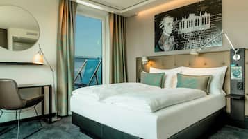 Hotelkamer met een groot bed, een bureau, een stoel, een spiegel, een raam met gordijnen en een wanddecoratie.