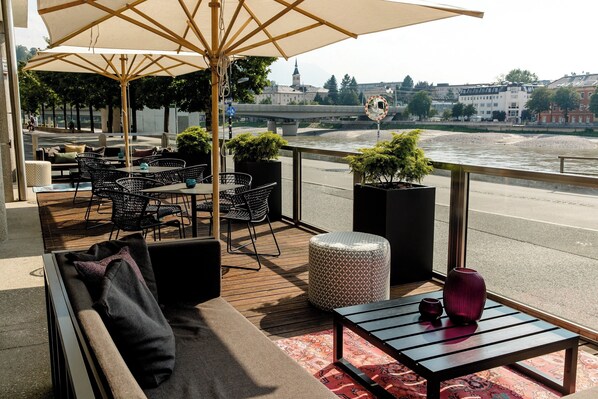 Una terraza con mesas al aire libre, vista de un río y un puente al fondo.