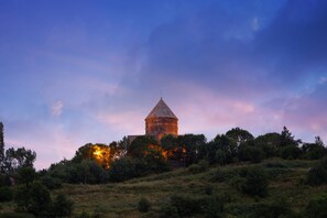 A historical tower with a conical roof, surrounded by dense greenery and trees, set against a twilight sky. - Tsaghkadzor Marriott Hotel (Tsaghkadzor)