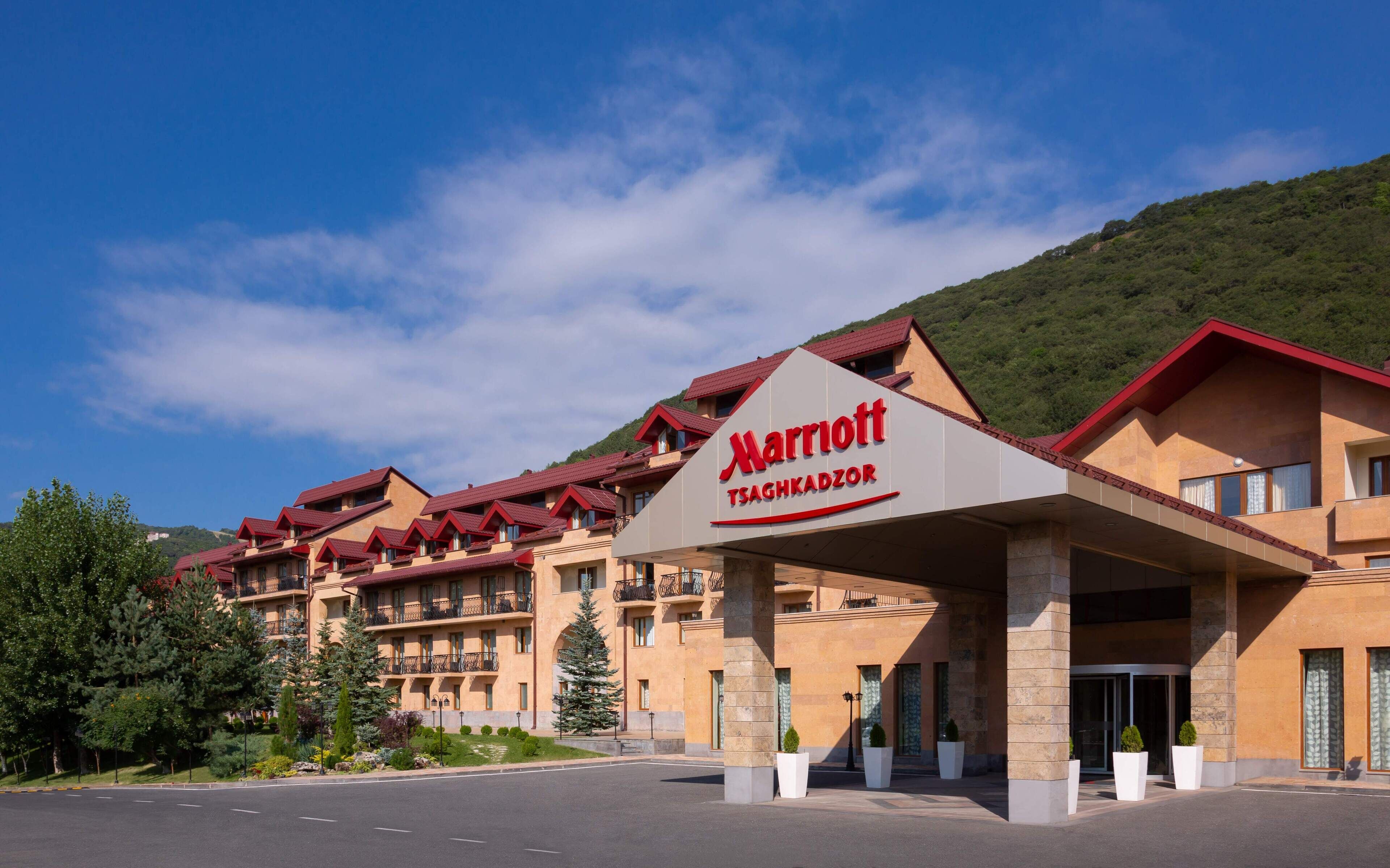 A Marriott hotel with a red and beige facade, multiple balconies, and a mountainous backdrop.