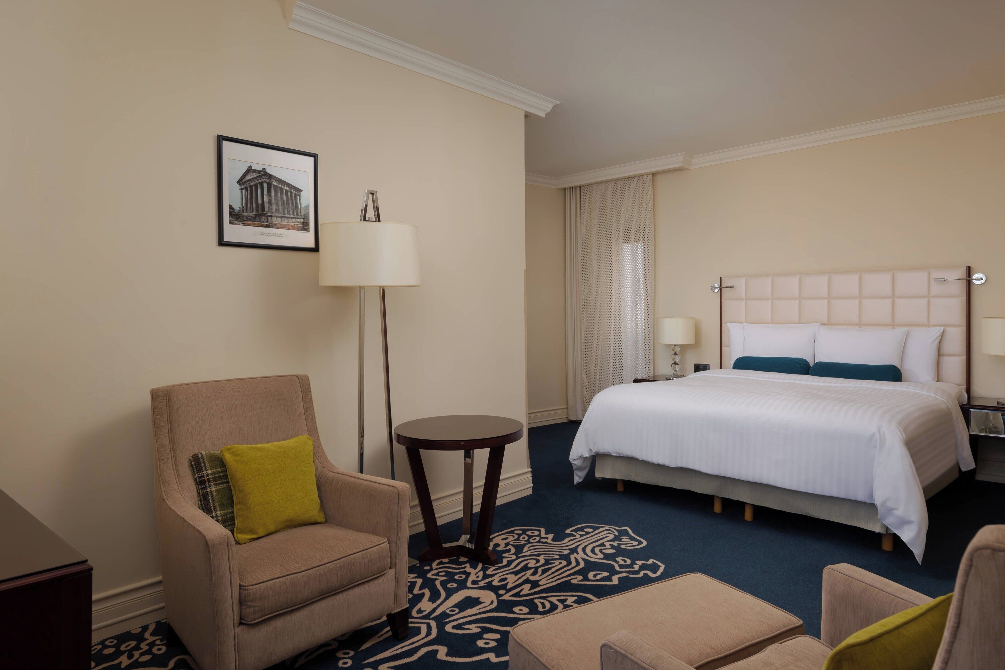 A hotel room with a bed, a chair, a small table, and a lamp.