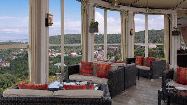A sunroom with large windows, wicker furniture, and a view of a green landscape. - Tsaghkadzor Marriott Hotel (Tsaghkadzor)