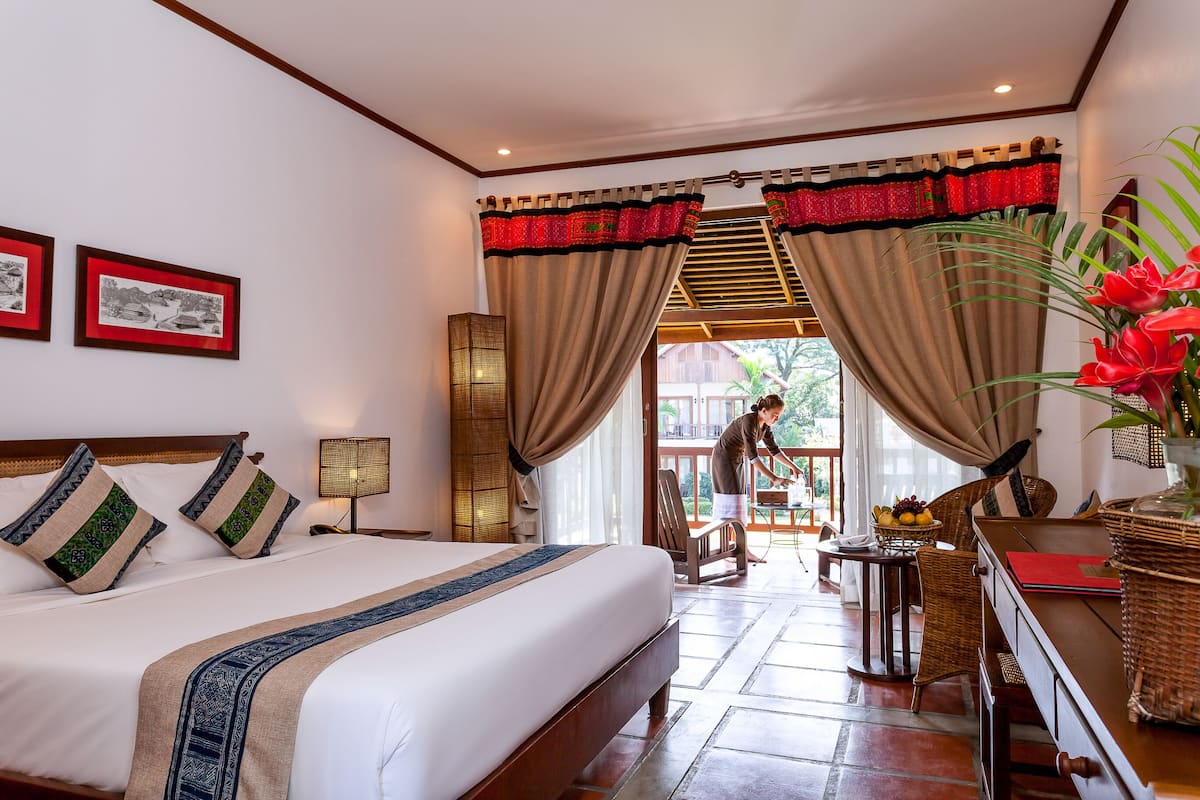 Une chambre d’hôtel avec un grand lit, une table à manger avec des chaises, une petite table avec un panier de fruits et une vue sur l’extérieur.