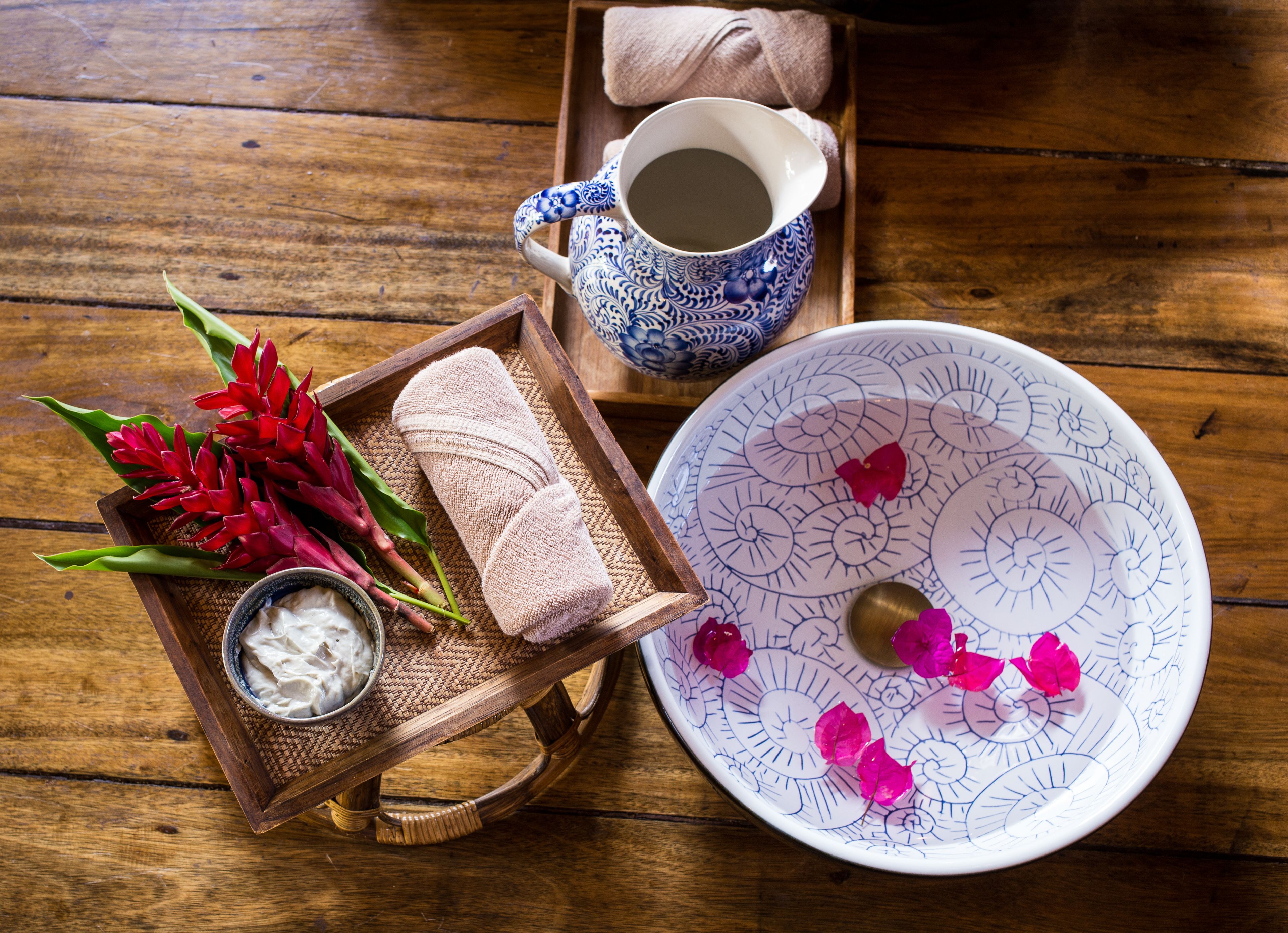 Un plateau en bois avec un bol de yaourt, une théière bleue et blanche, une serviette enroulée et des fleurs rouges.