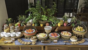 Une table de buffet proposant une variété d’aliments, notamment des fruits, des légumes et des céréales, disposés sur une nappe à motifs.