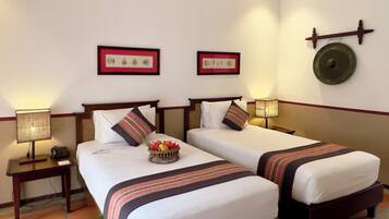 A hotel room with two beds, a bedside table with a lamp, a wall clock, and framed artwork.
