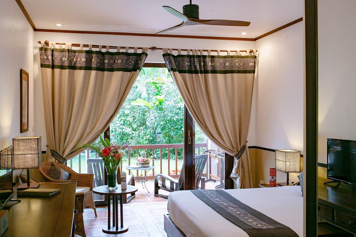 Une chambre d’hôtel comprenant un lit, un bureau, une chaise, une petite table avec un vase de fleurs et un balcon avec une table et des chaises.