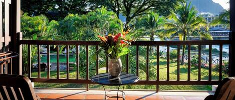 A balcony with a view of a lush garden and a body of water.