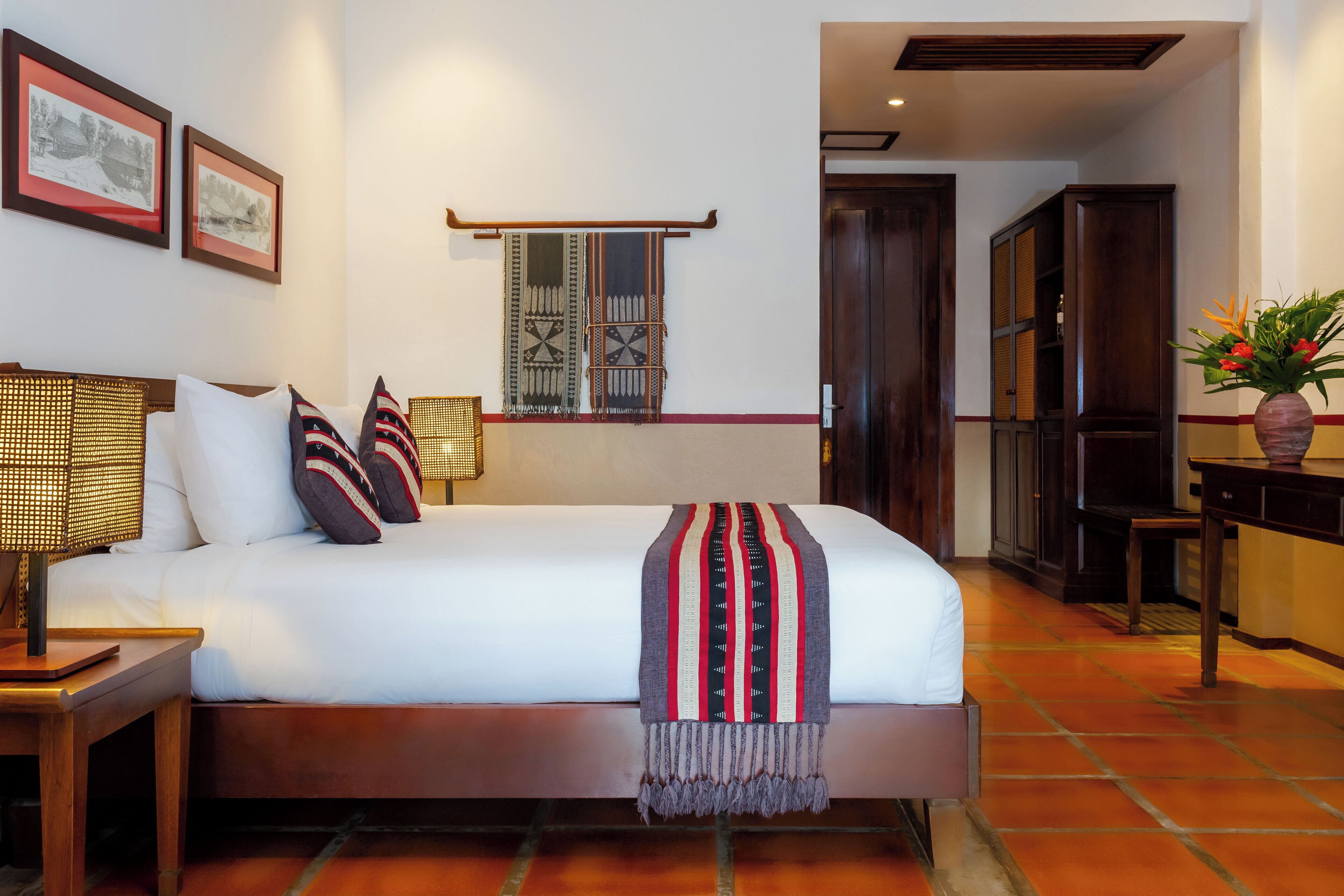 Un dormitorio con cama, mesitas de noche, lámpara, estante en la pared y ventana con cortinas estampadas.