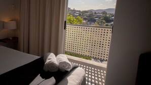 A hotel room with a bed, a nightstand, a lamp, and a window with a view of a cityscape. - Herston Place Motel (Herston)