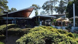 A modern outdoor seating area with a covered patio, surrounded by well-maintained bushes and trees. - Herston Place Motel (Herston)