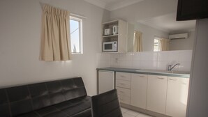 A compact kitchenette with a microwave, a sink, and a window with curtains. - Herston Place Motel (Herston)