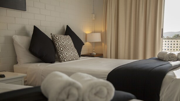A hotel room with two beds, a nightstand, a lamp, and a window with curtains. - Herston Place Motel (Herston)