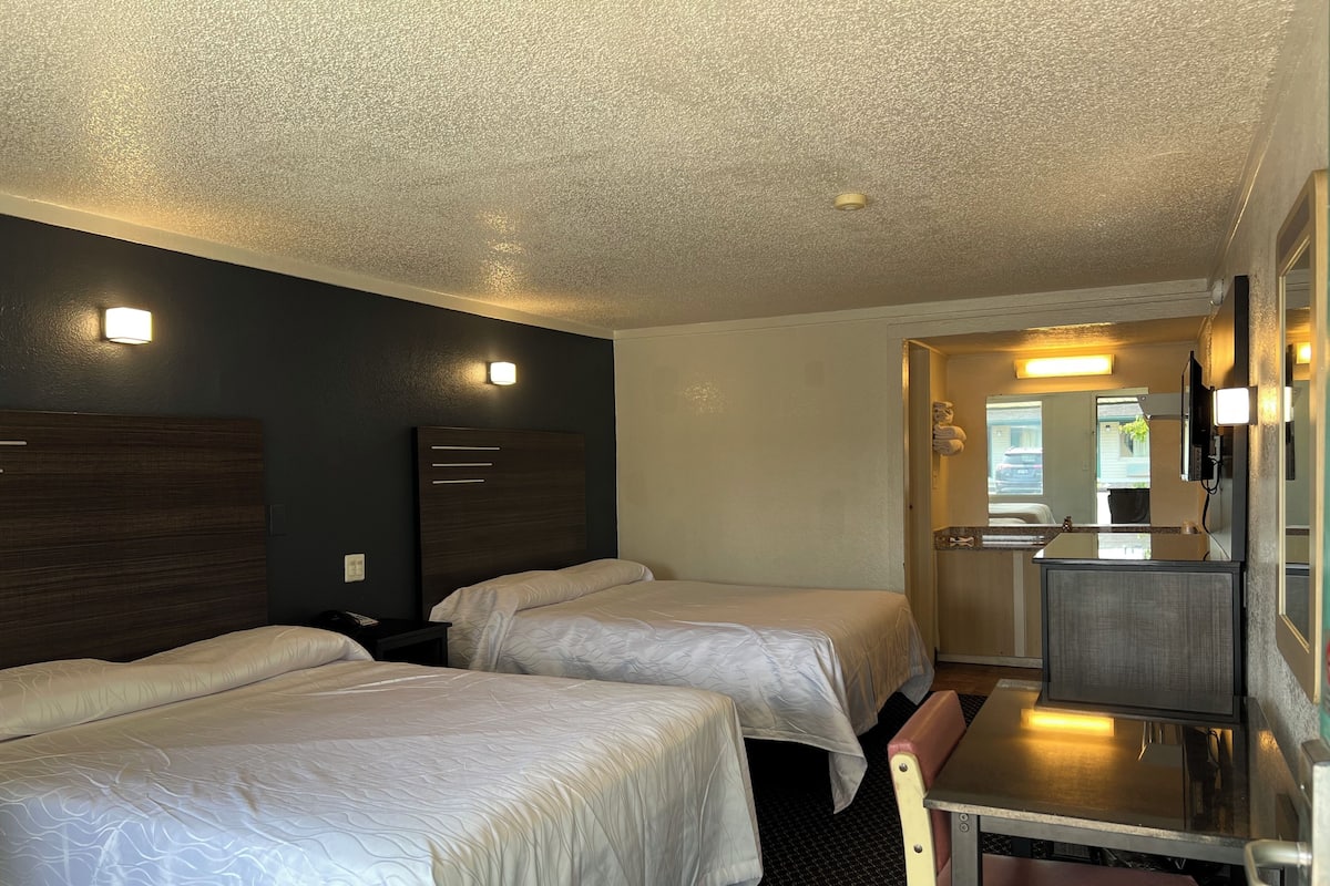 A hotel room with two beds, a desk, and a mirror.