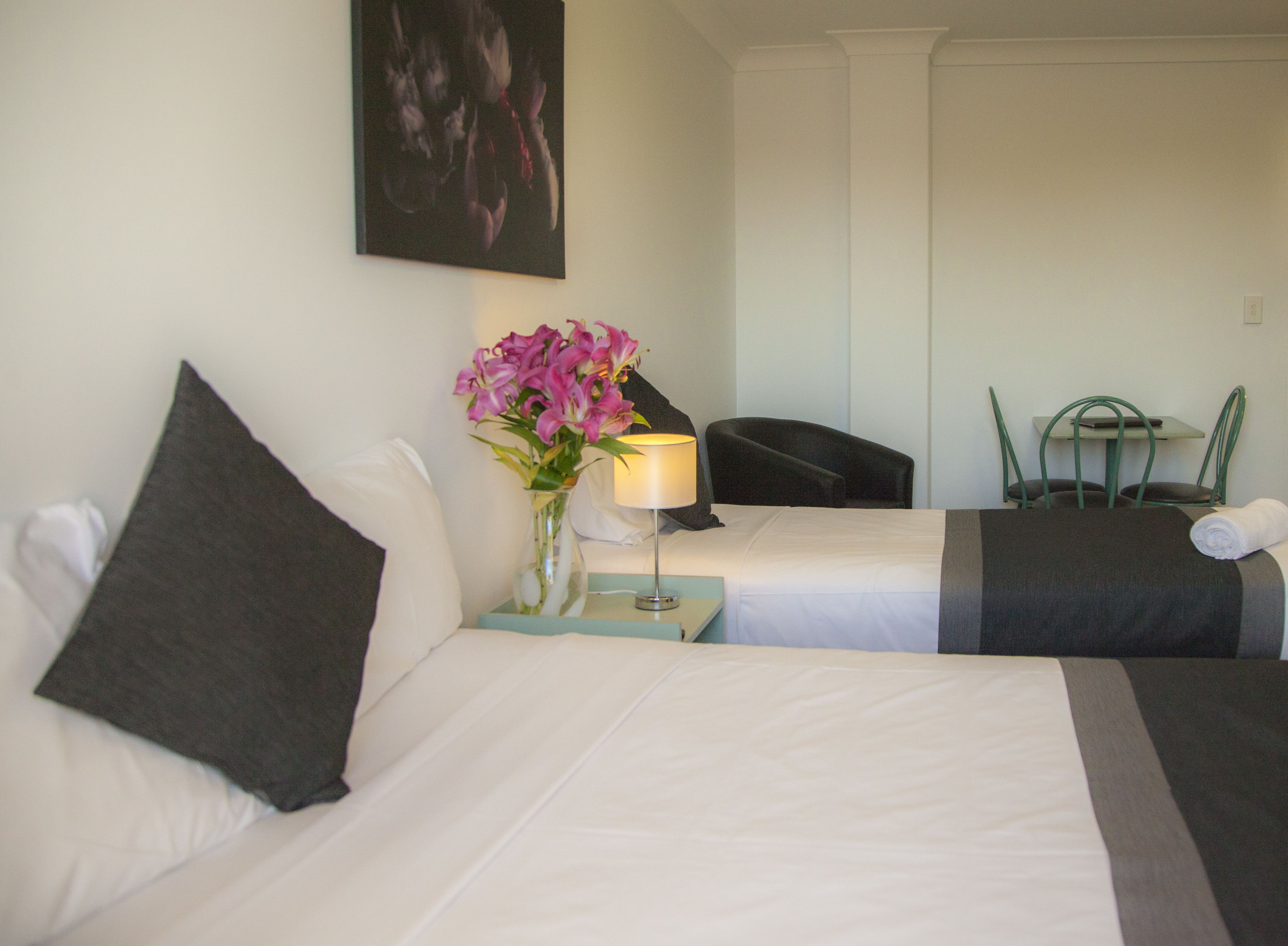 A hotel room with two beds, a vase of flowers, a lamp, a chair, and a table.