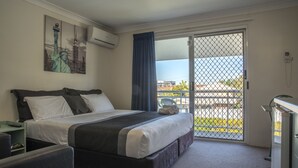 A hotel room with a bed, a desk, a chair, a painting of the Statue of Liberty, and a balcony with a view. - Chermside Court Motel (Chermside)