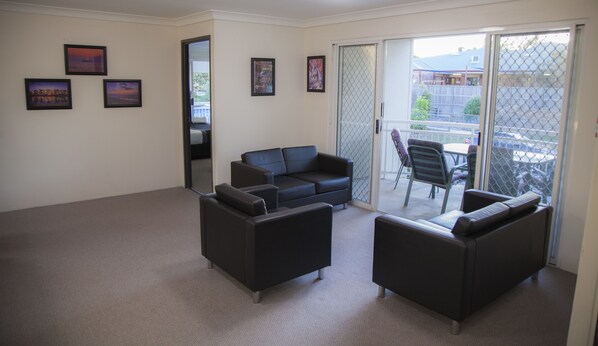 Amplia sala de estar con sofá negro, mesa de comedor con sillas y puerta corrediza de vidrio a un patio exterior.