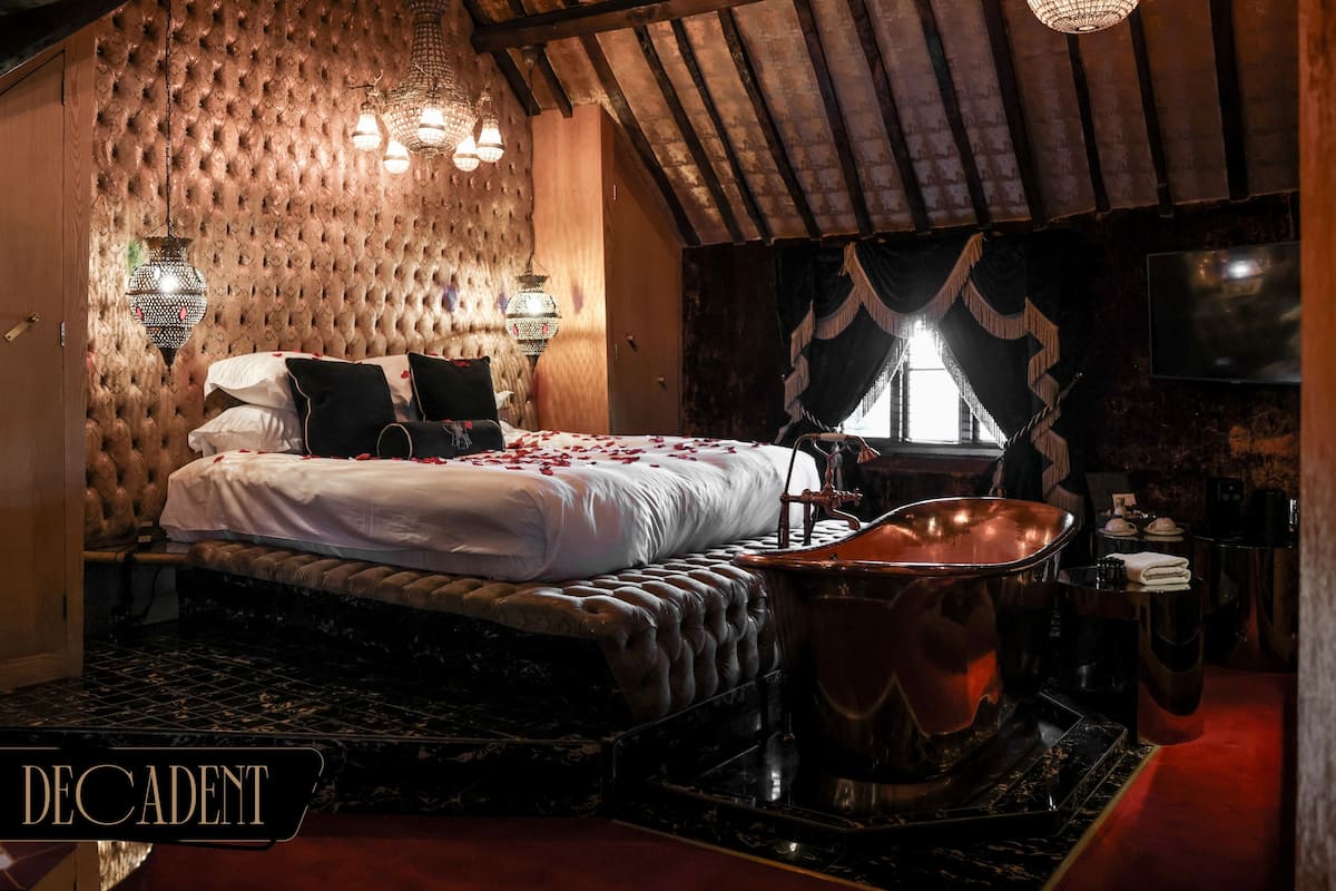 A bedroom with a large bed, a bathtub, and a chandelier.