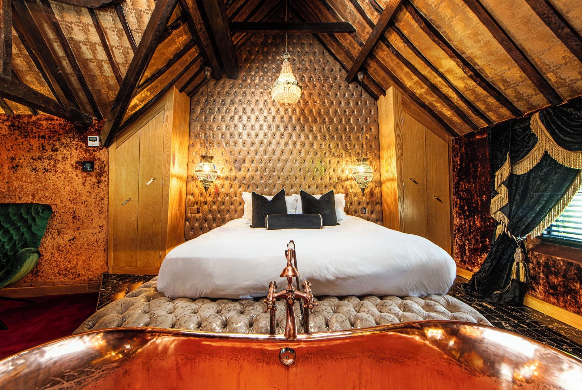A room with a bed, a chandelier, and a unique copper bathtub.
