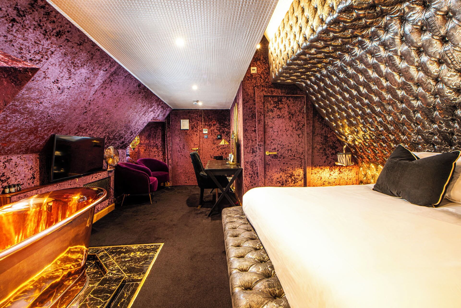 A room with a bed, a desk, a chair, a television, and a bathroom area.