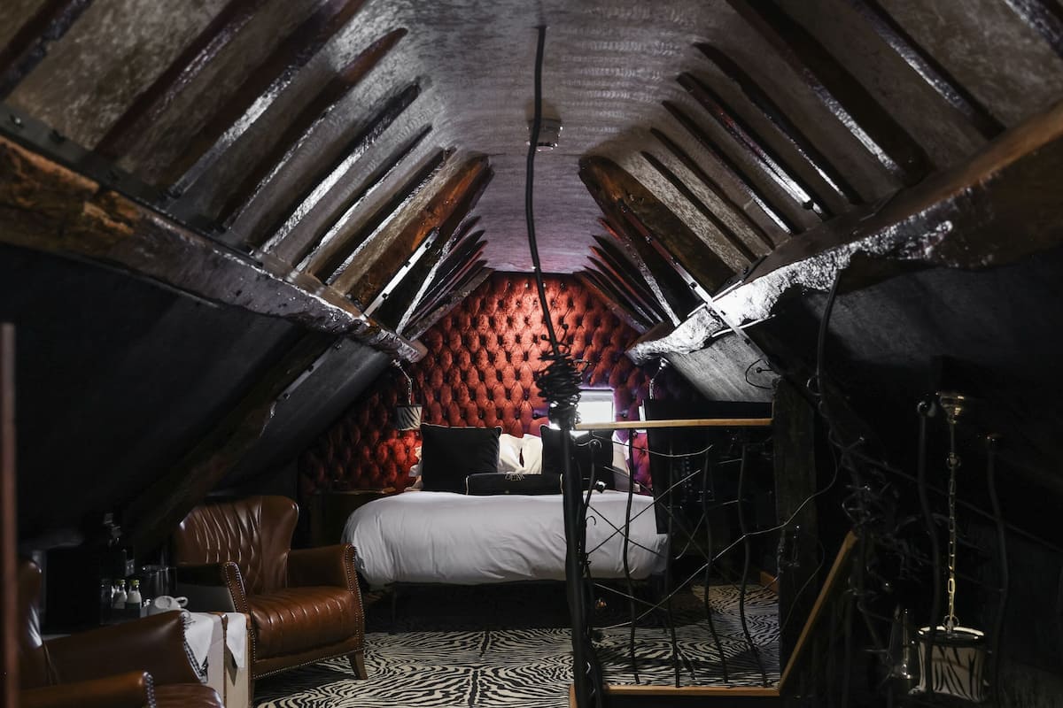 A room with a sloped ceiling, a bed with white bedding, a leather armchair, and a zebra-patterned rug.