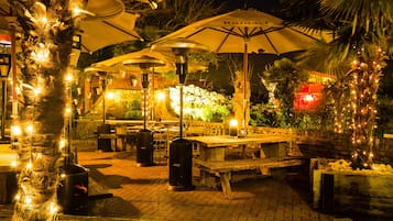 Ein Außenbereich mit Terrasse, Tischen, Stühlen, Sonnenschirmen und dekorativer Beleuchtung.