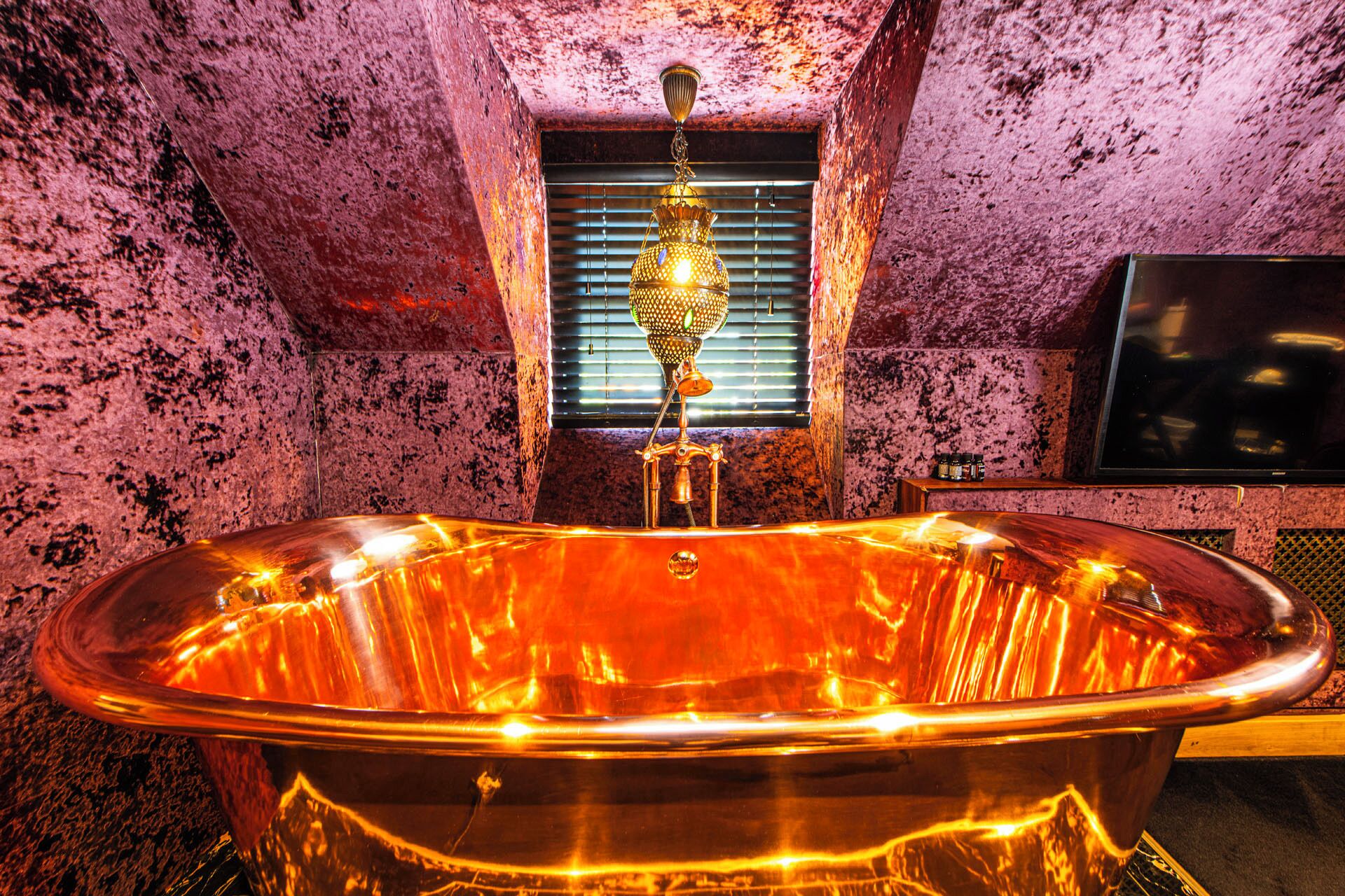 A bathtub with a faucet and a window with blinds.