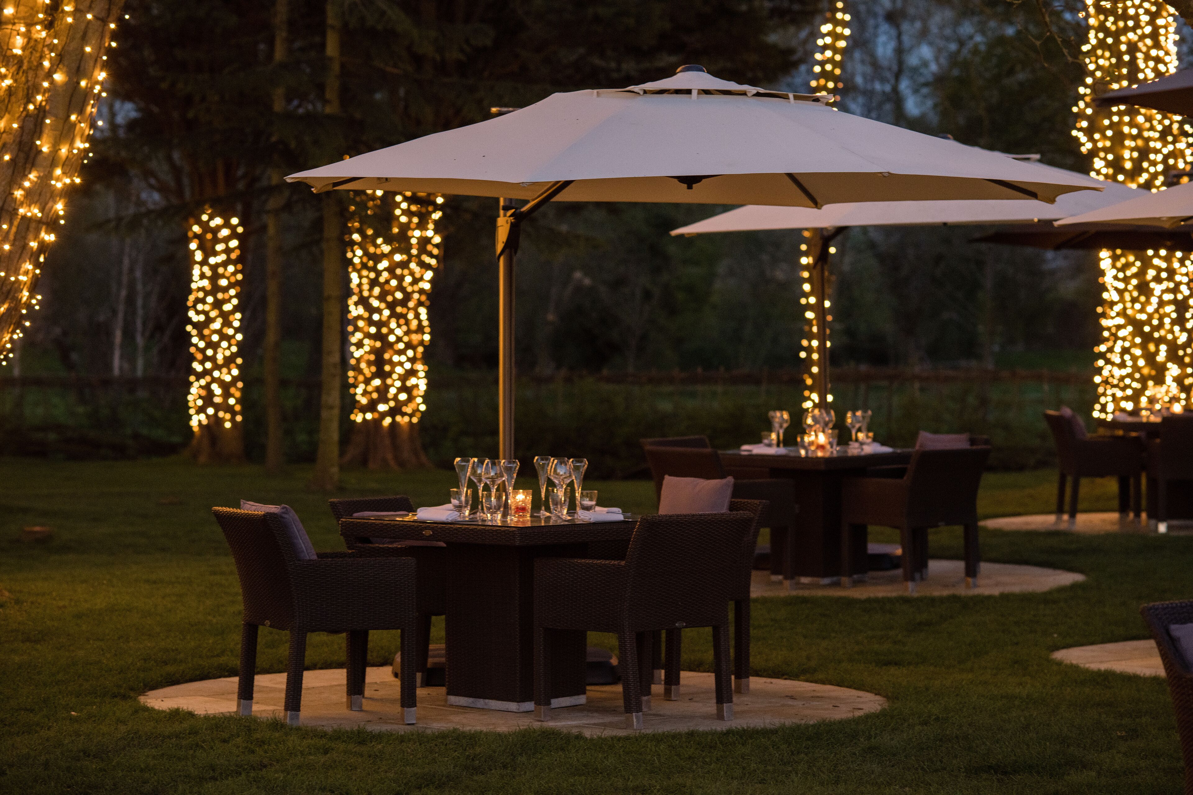 An outdoor dining area with tables and chairs, surrounded by string lights.