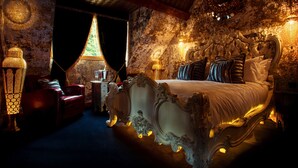 Ein luxuriöses Schlafzimmer mit einem großen, verzierten Bett, einem roten Ledersessel und einer Kristallleuchter.