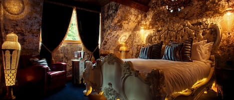 Un dormitorio lujoso con una cama grande y ornamentada, un sillón de cuero rojo y una araña.