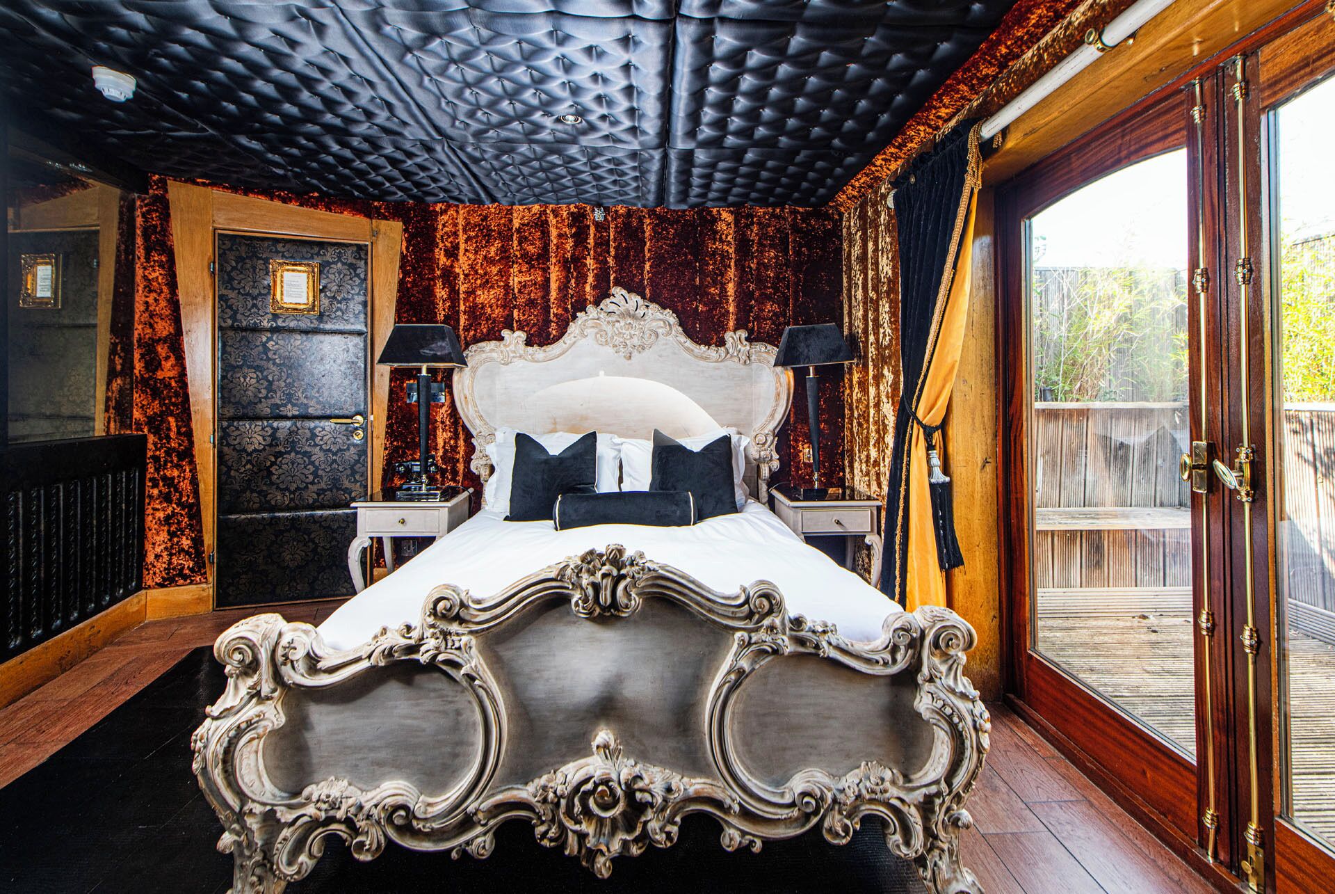 A bedroom with a large bed, ornate headboard, and a view of a wooden deck.