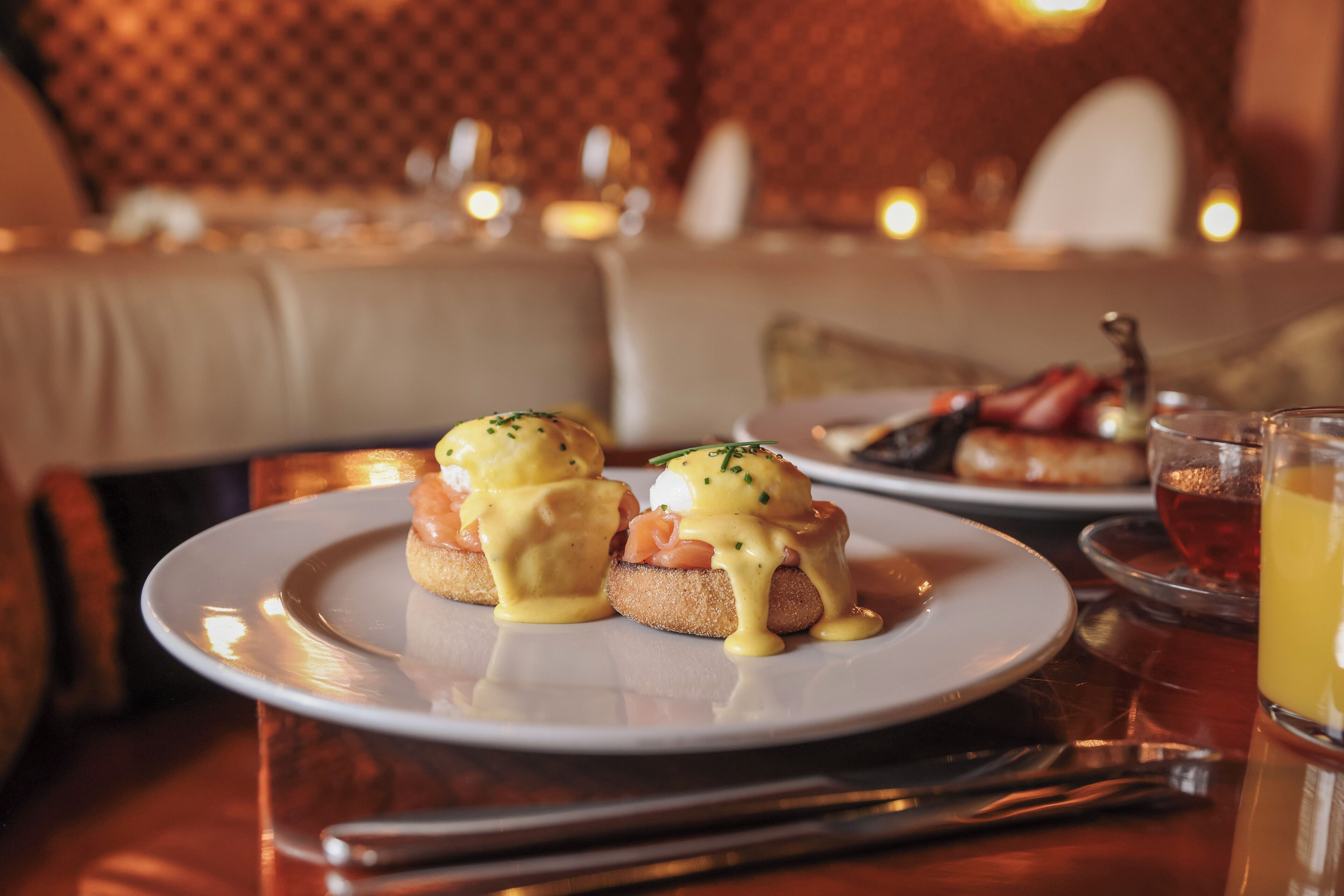 A dining table with a plate of eggs benedict and a glass of juice.