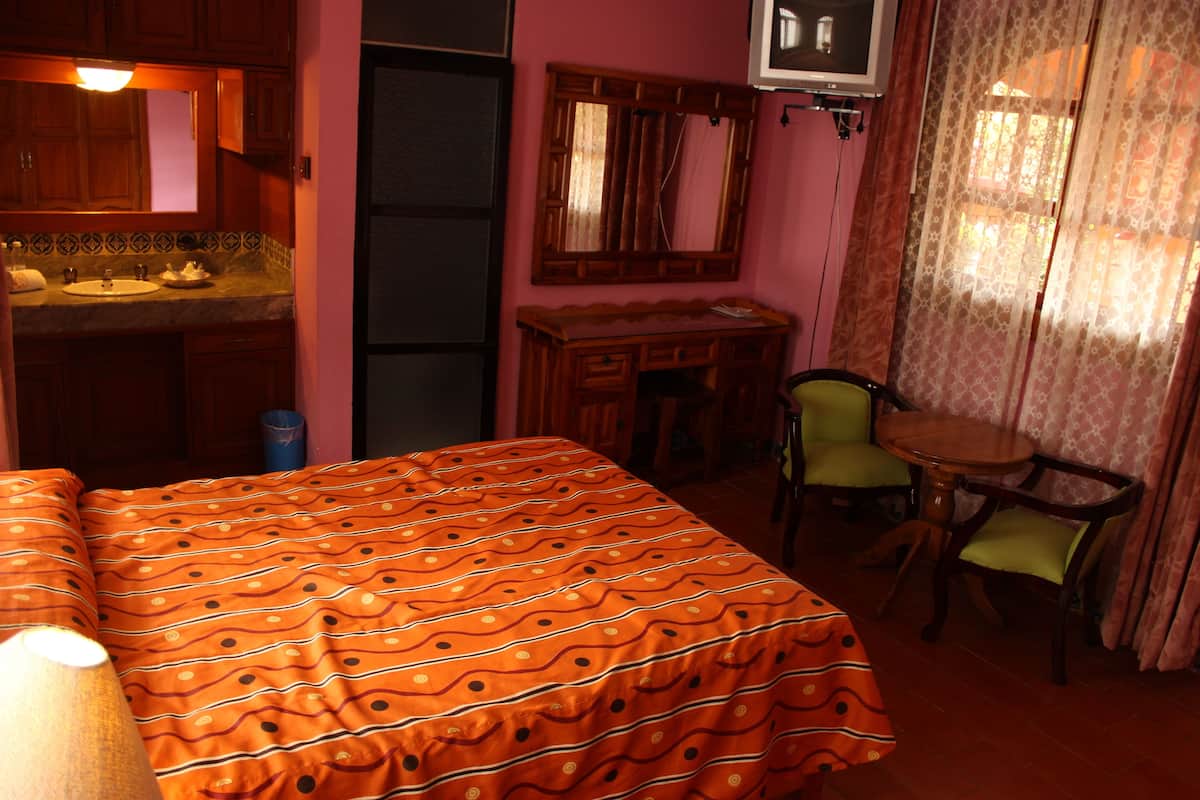 Ein Zimmer mit einem Bett, einem Schreibtisch, einem Stuhl, einem kleinen Tisch, einem Spiegel und einem Waschbecken.