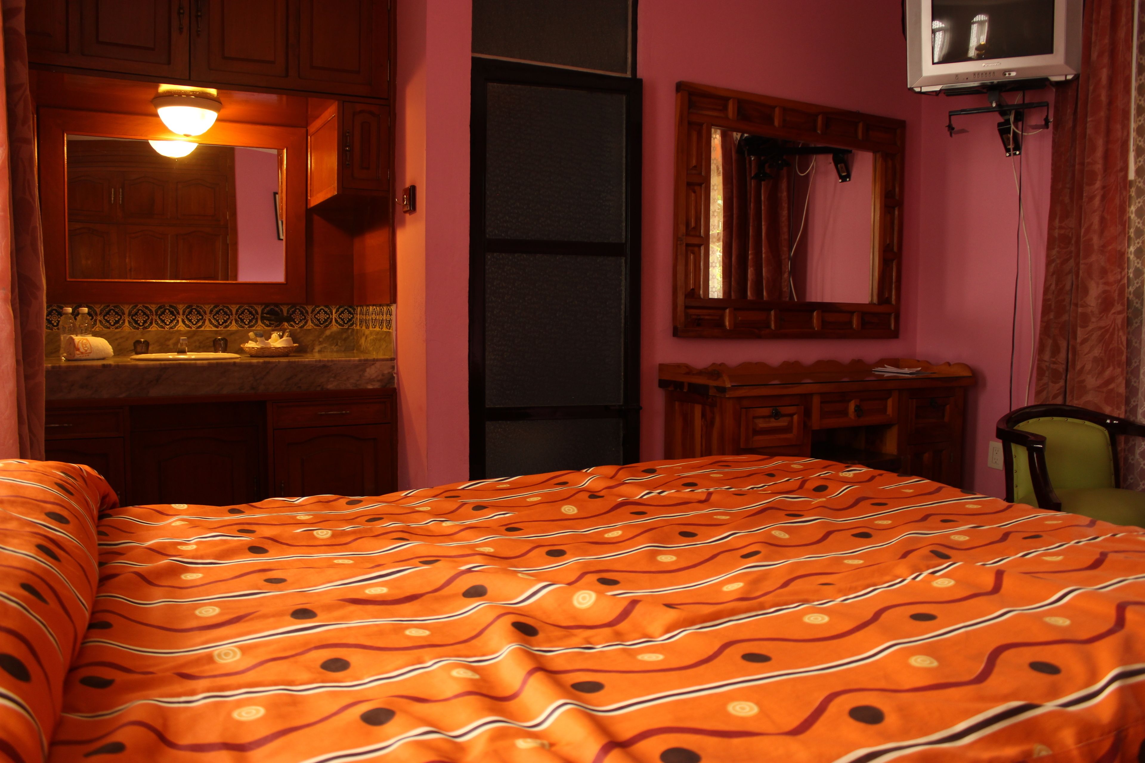 A bedroom with a bed, a dresser, a mirror, and a television.