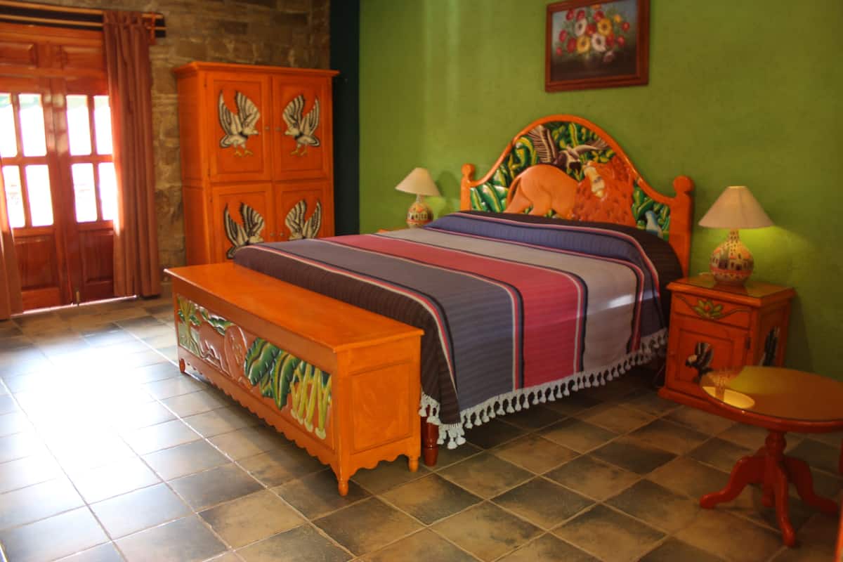 Ein Schlafzimmer mit Bett, Holzschrank, Bank und kleinem Tisch.
