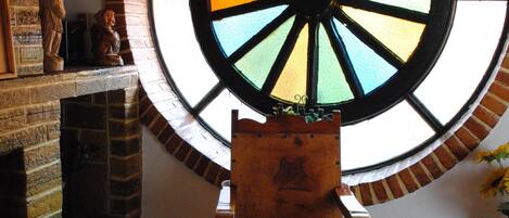 A room with a large circular stained glass window, a wooden chair, and a brick fireplace.