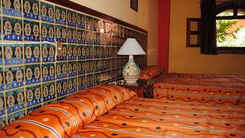 A room with a tiled wall, a bed with patterned bedding, a lamp, and a window with curtains.